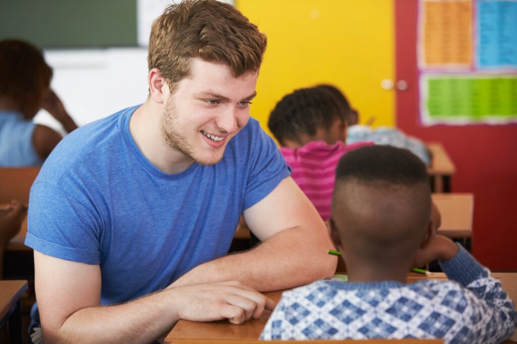 White male Volunteer teacher helping boy in elementary school class